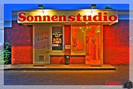 Außenansicht eines Sonnenstudios mit beleuchtetem Schild und rotem Ziegelstein.