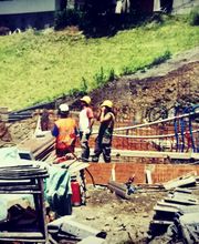 Bauarbeiter mit Schutzhelmen arbeiten auf einer Baustelle im Freien. Um sie herum sind Baugerüste.