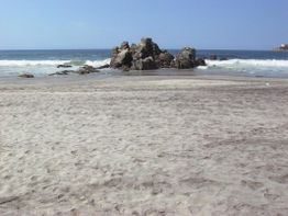 Sandstrand mit Felsen im Meer unter klarem, blauem Himmel.