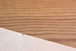 Holzoberfläche mit diagonaler Kante, darunter eine glatte, weiße Fläche.