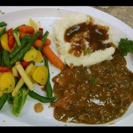 Mashed potatoes with gravy, beef steak in sauce, and colorful steamed vegetables on a white plate.