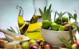 Caraffa di olio d'oliva con ciotola di olive verdi e nere su un tavolo, vicino a pane e cucchiaio.