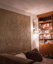 Wohnzimmer mit braunem Sofa, Bücherregal, Lampe und einem Hund auf dem Boden.