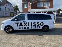Weißer Kleinbus mit der Aufschrift "Taxi Isso" und Telefonnummer auf einem Parkplatz.