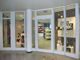 Geschäft mit Glasfassade, Auslagen mit Schmuck und Kleidung, beleuchtet, moderner Innenraum.