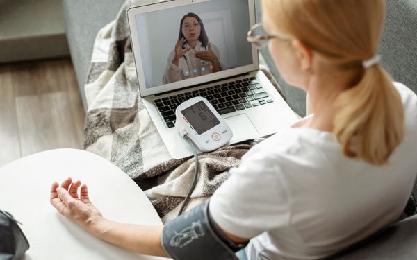 Frau misst zu Hause ihren Blutdruck während einer Videosprechstunde mit einer Ärztin am Laptop.