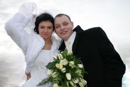 Ein Brautpaar lächelt in die Kamera. Die Braut trägt ein weißes Kleid, der Bräutigam einen Anzug.