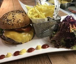Burger mit Pommes und Salat auf einem weißen Teller, dekoriert mit Ketchup und Senf-Tupfen.