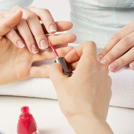 Applying red nail polish to fingernails on a white towel background.
