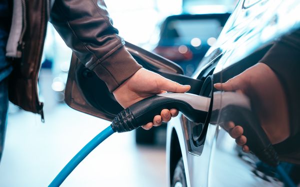 Ein Mann steckt den Ladestecker in den Ladeanschluss seines Elektroautos.