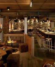 Gemütliche Bar im rustikalen Stil mit Holzmöbeln, Steinwänden und einer langen Theke.