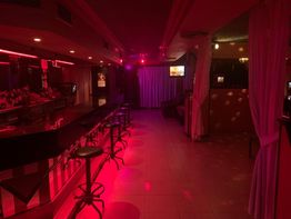 Bar de ambiente nocturno con iluminación roja y sillas altas frente a la barra.