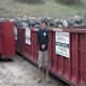 Man standing near large red waste containers labeled "R.B. and Sons Services."