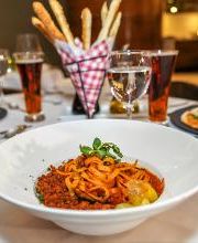 Plato de pasta con salsa, rodeado de pizzas, copas de vino y cervezas en una mesa elegante.