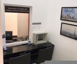 Sala de espera com balcão, duas cadeiras e fotos na parede. Janela de atendimento à esquerda.