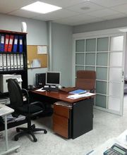 Oficina moderna con escritorios, sillas ergonómicas, archivadores y puerta corrediza de vidrio.