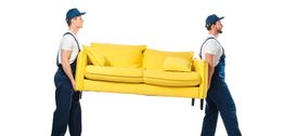 Zwei Männer in Arbeitskleidung tragen ein gelbes Sofa mit einem Kissen.