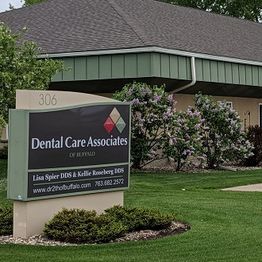 Dental Care Associates sign outside a building with flowering bushes and a green lawn.