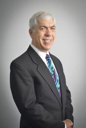 Smiling man in a suit with a colorful tie, standing against a gray background.