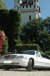 Weiße Limousine vor einem hohen, bewachsenen Turm an einem sonnigen Tag.