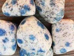 Speckled stones with blue spots on a wooden surface.