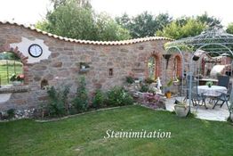 Garten mit Steinmauer, Uhr und Pavillon. Blumentöpfe und grüne Rasenfläche im Vordergrund.