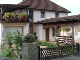 Zweistöckiges Haus mit Balkon, Blumenbeeten und Holzzaun im Vorgarten.