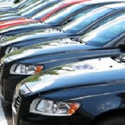 Row of parked cars in various colors, mainly black and red, viewed from the front angle.