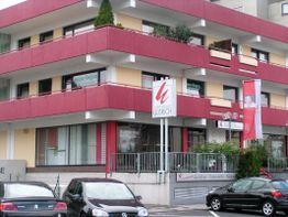 Mehrstöckiges Gebäude mit roten Balkonen und mehreren Autos im Vordergrund.