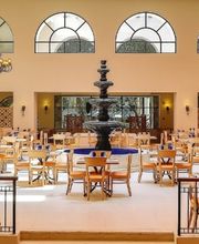 Restaurante elegante con mesas de madera, fuentes y ventanales amplios.