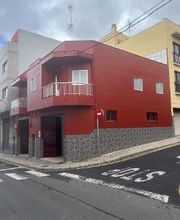 Edificio rojo en esquina de calle con señales de tráfico, cielo nublado.