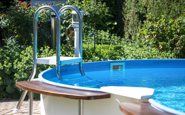 Ein Aufstellpool mit Stahlwand mit blauem Wasser, in einem blühenden Garten.