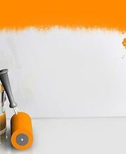 Farbeimer mit orangener Farbe und Rolle vor weißer teils orangener Wand.