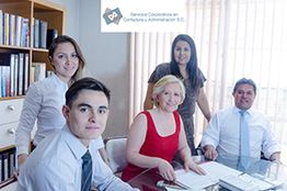 Cinco personas en una reunión de oficina, con logo de consultoría al fondo.