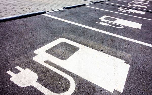 Parkbuchten für Elektrofahrzeuge. Auf der geteerten Fläche wird durch eine Abbildung klar gemacht, dass sich hier eine Ladesäule für Elektrofahrzeuge befindet.