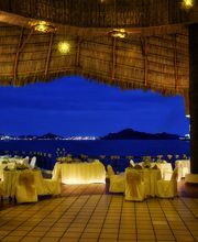 Restaurante al aire libre con mesas decoradas, vista al mar y luces cálidas de noche.
