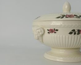 Witte soepterrine met bloemmotief en decoratief detail op een grijze achtergrond.