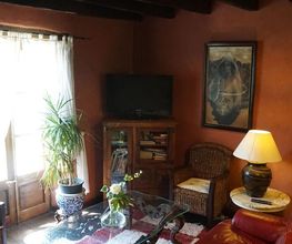 Sala de estar rústica con sofá rojo, mesa de cristal, plantas y lámpara de mesa junto a ventana.