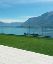 Terrasse mit Glasgeländer, Blick auf See und Berge unter blauem Himmel.