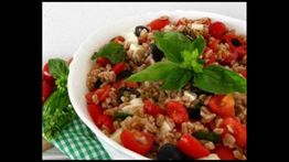 Ciotola di insalata di farro con pomodorini, basilico e mozzarella. Decorata con foglie di basilico.