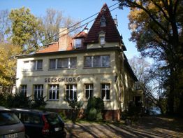 Gelbes Gebäude mit Schriftzug "Seeschloss", umgeben von Bäumen, Autos parken davor.