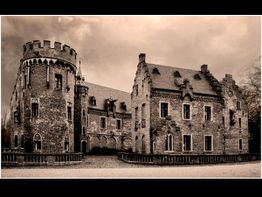 Historisches Schloss aus Backstein mit Türmen und Zinnen unter einem wolkenverhangenen Himmel.