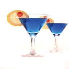 Zwei blaue Cocktails in Martini-Gläsern mit Zitronenscheiben und Kirsche garniert.