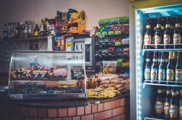 Small shop with a glass counter of sweets and a fridge stocked with various bottled drinks.