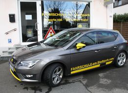 Graues Fahrschulauto vor einem Gebäude mit der Aufschrift "Fahrschule am Stadtpark".