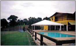 Casa com piscina e jardim, cercada por árvores, céu nublado.