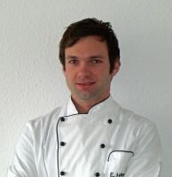 Ein Koch in weißer Uniform steht vor einer weißen Wand.