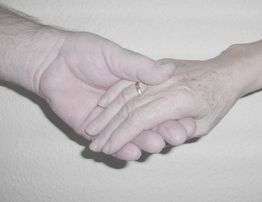 Zwei Hände im Händedruck, eine mit einem Ring, vor einem neutralen Hintergrund.