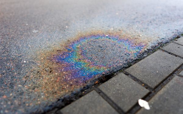 Ein bunter Ölfleck auf einer Straße, verursacht durch ein Auto mit Leck im Öltank.
