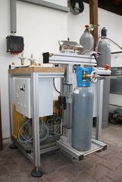 Maschine zur Gasabfüllung, mit grauen Gasflaschen und Steuerungen in einem industriellen Raum.